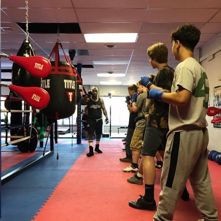 Beginner boxing class in session with a coach instructing students near the heavy bags